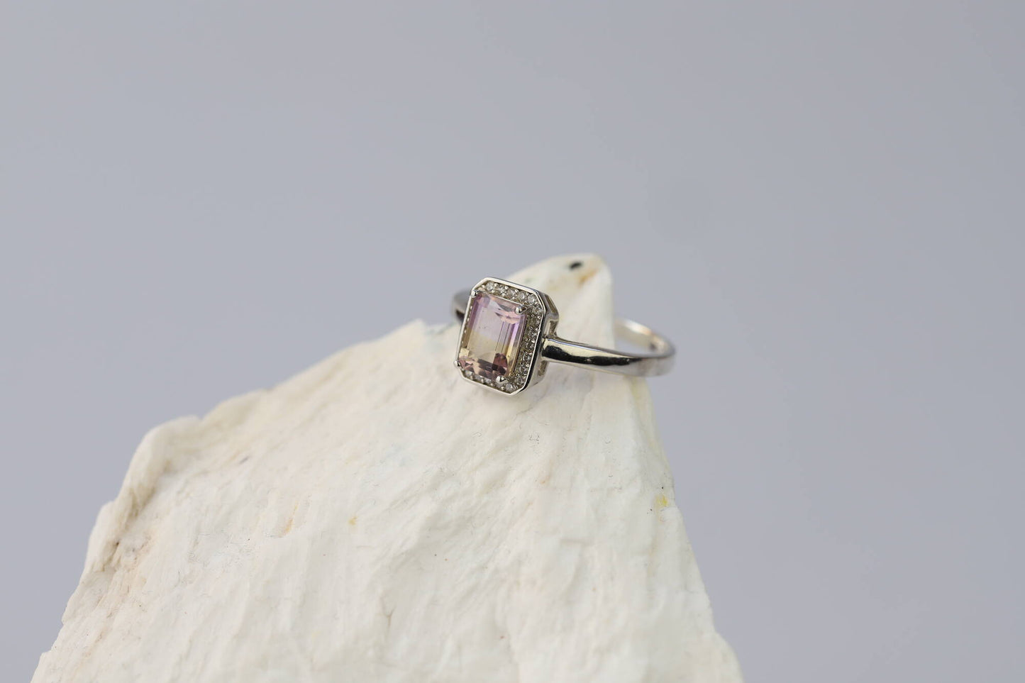 Kristallwerk präsentiert: Ring mit facettiertem Amethyst-Edelstein und umringt mit kleinen Bergkristallen aus Silber 925 auf weissem Stein.