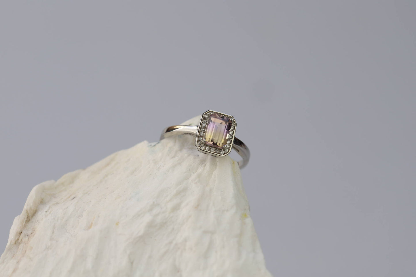 Kristallwerk präsentiert: Ring mit facettiertem Amethyst-Edelstein und umringt mit kleinen Bergkristallen aus Silber 925 auf weissem Stein.