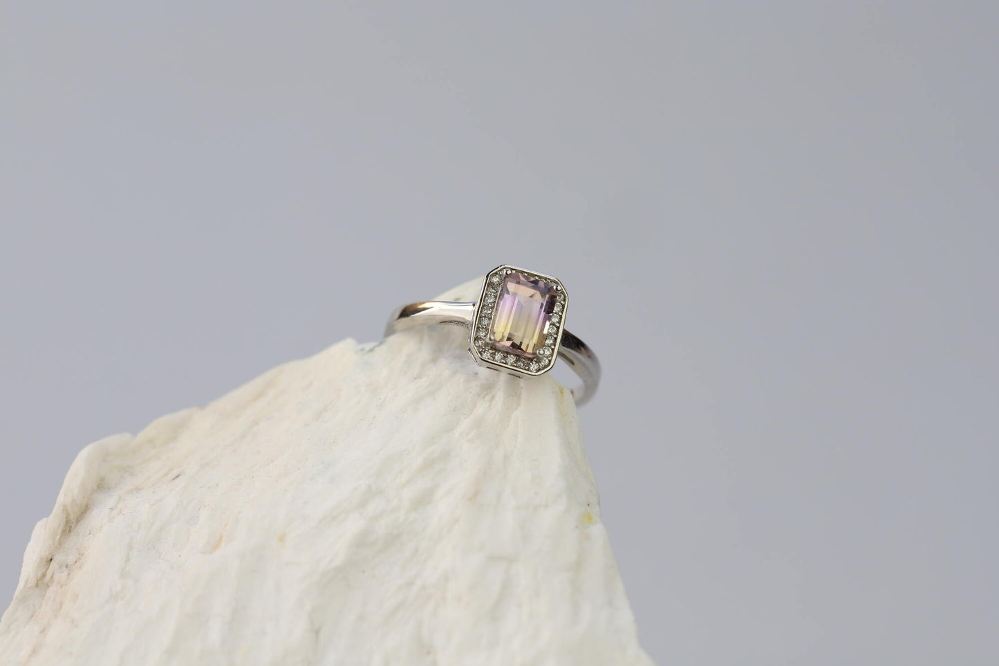 Kristallwerk präsentiert: Ring mit facettiertem Amethyst-Edelstein und umringt mit kleinen Bergkristallen aus Silber 925 auf weissem Stein.